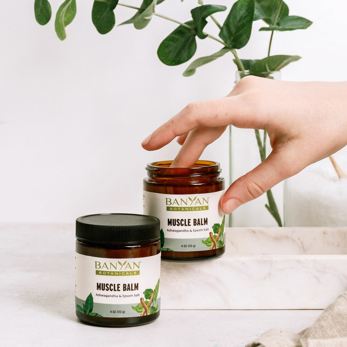 Two jars of muscle balm with someone using one